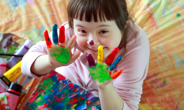 A girl smiles with her hands covered in brightly coloured paint