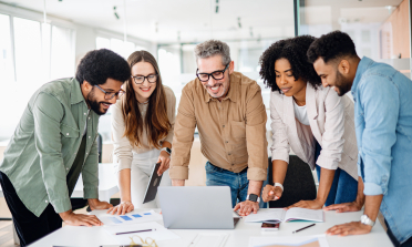 Five adults stand around a laptop on a table