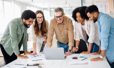 Five adults stand around a laptop on a table