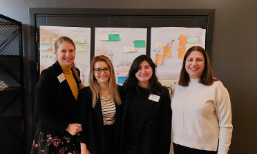 Four members of the project team stand in front of a display board