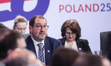 João Costa speaking in front of a sign saying Poland 25