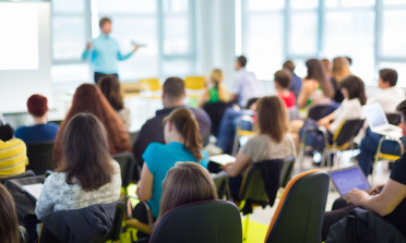 People in a conference room listening to someone speaking at the front