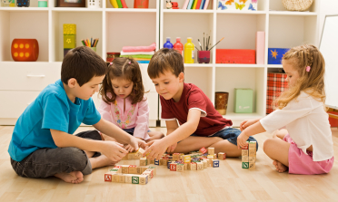 Four children play with building blocks that have numbers and letters on them