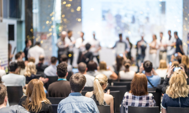 People sit watching other people on the stage at the front