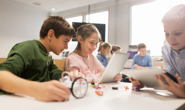 Two children look at a computer screen, one holding a magnifying glass