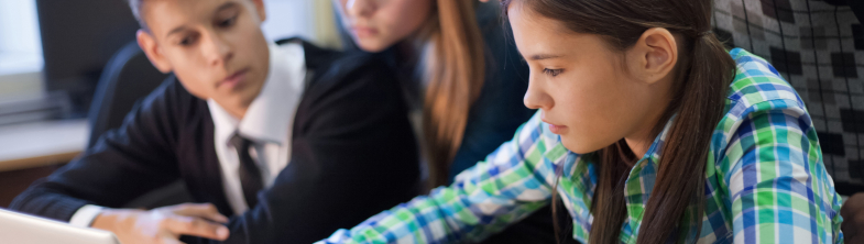 Three teenagers look at a laptop on a desk with their teacher