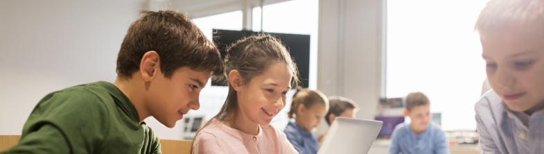 Two children look at a computer screen, one holding a magnifying glass