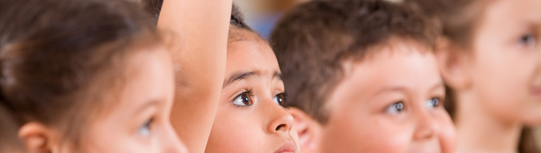 A group of children sitting together, a girl has her hand in the air