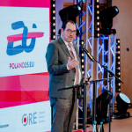 João Costa speaking on stage in front of a sign saying Poland 25