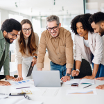 Five adults stand around a laptop on a table