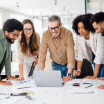 Five adults stand around a laptop on a table