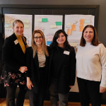 Four members of the project team stand in front of a display board