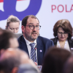 João Costa speaking in front of a sign saying Poland 25