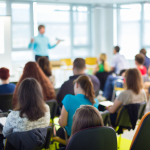 People in a conference room listening to someone speaking at the front