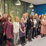 A group of people stand in front of wall with a picture of a forest of trees on it