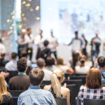 People sit watching other people on the stage at the front